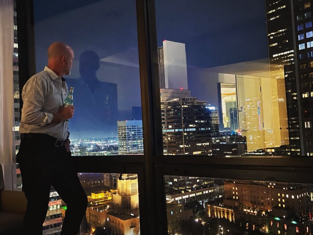 Peter Pendleton at a window overlooking downtown Los Angeles at night