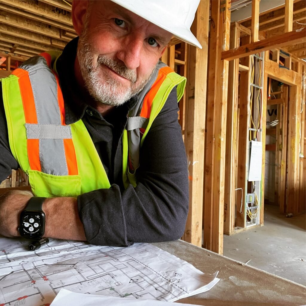 Peter Pendleton in a hard hat and safety vest reviewing plans on a framed jobsite